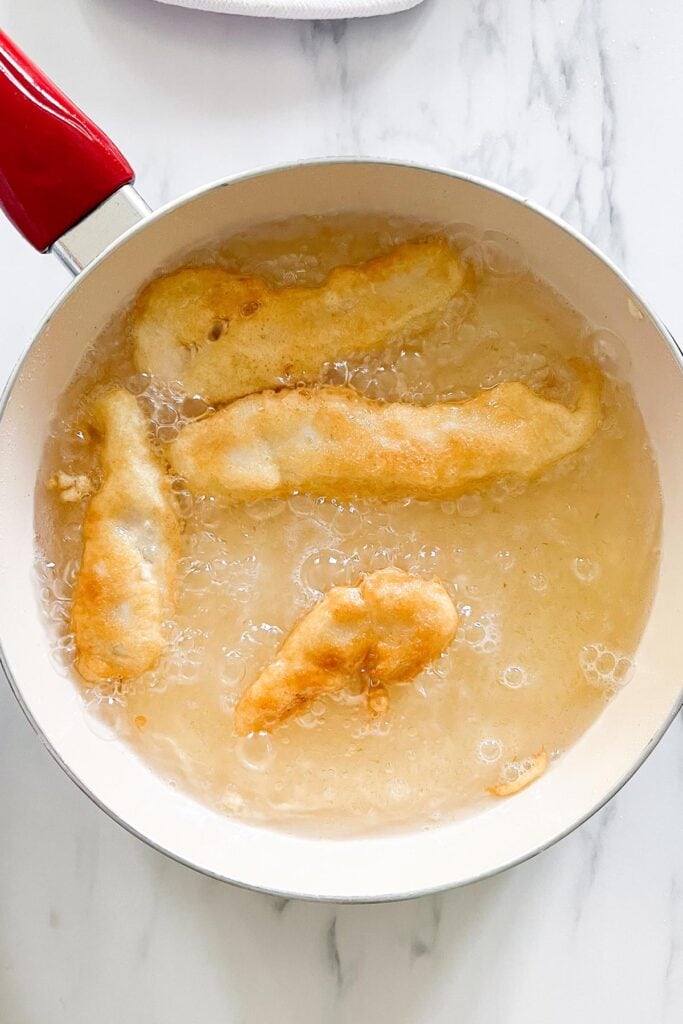 Battered fish frying in a pan.
