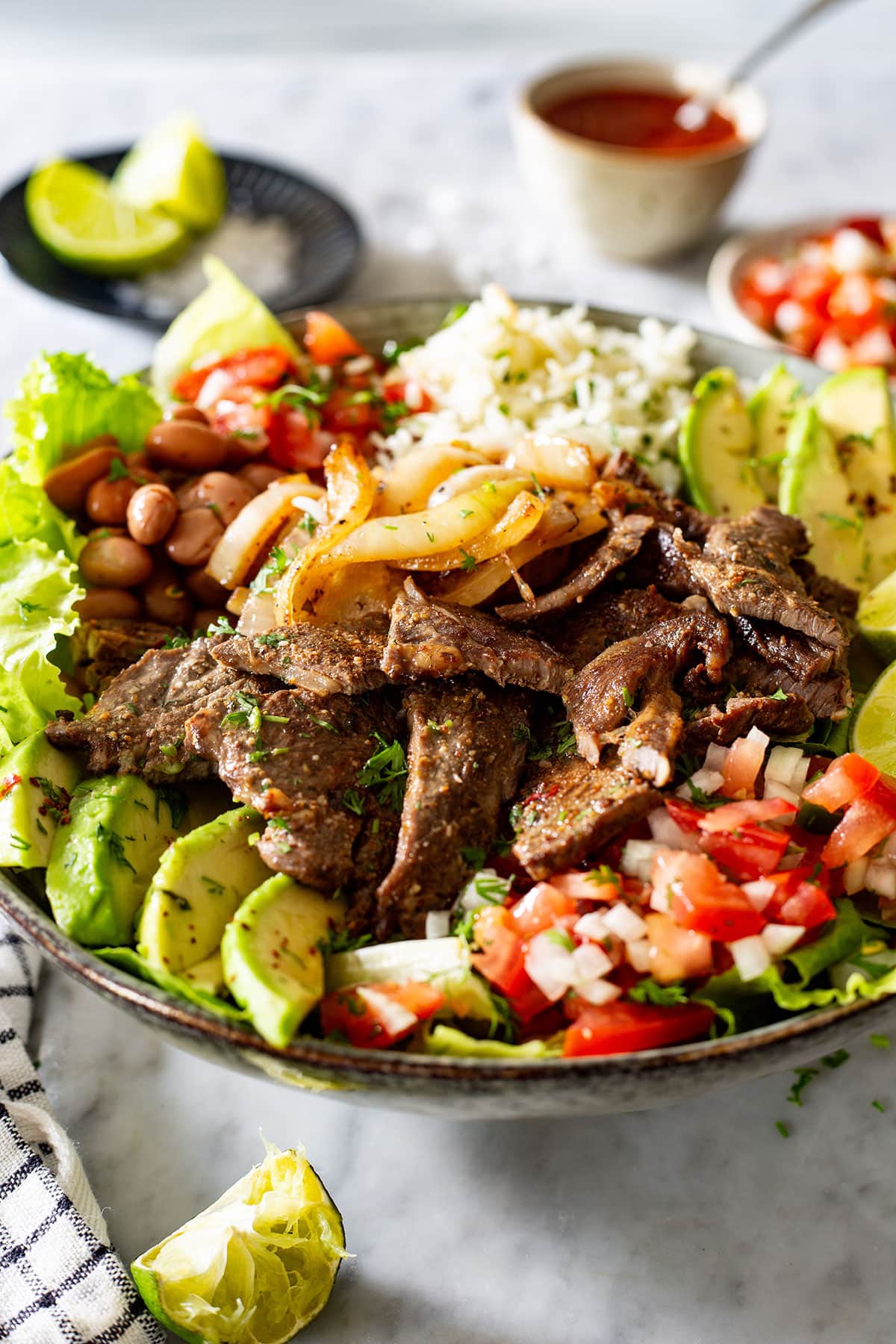 Carne asada bowl with salsa and lime wedges on the side.