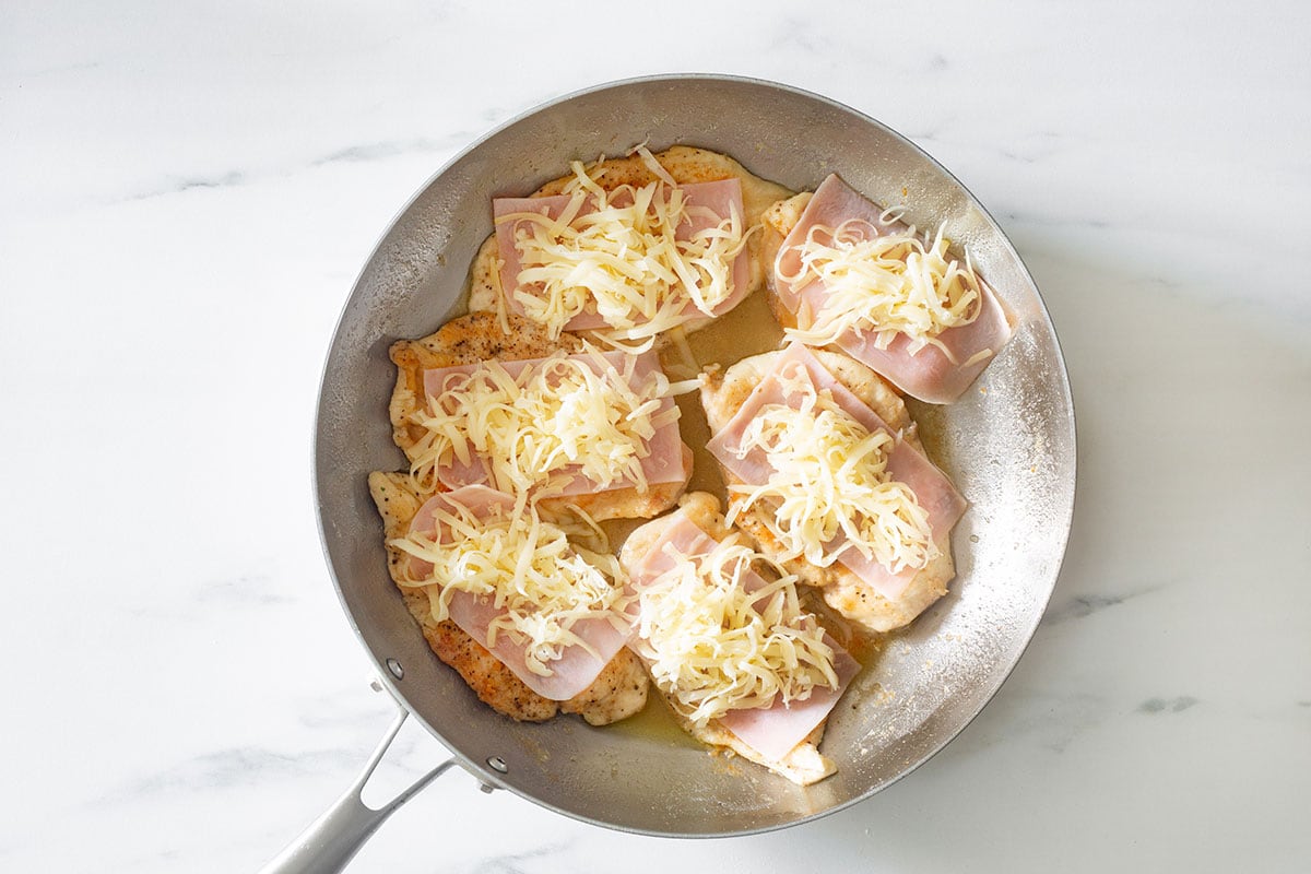 Chicken topped with ham and cheese in a pan.