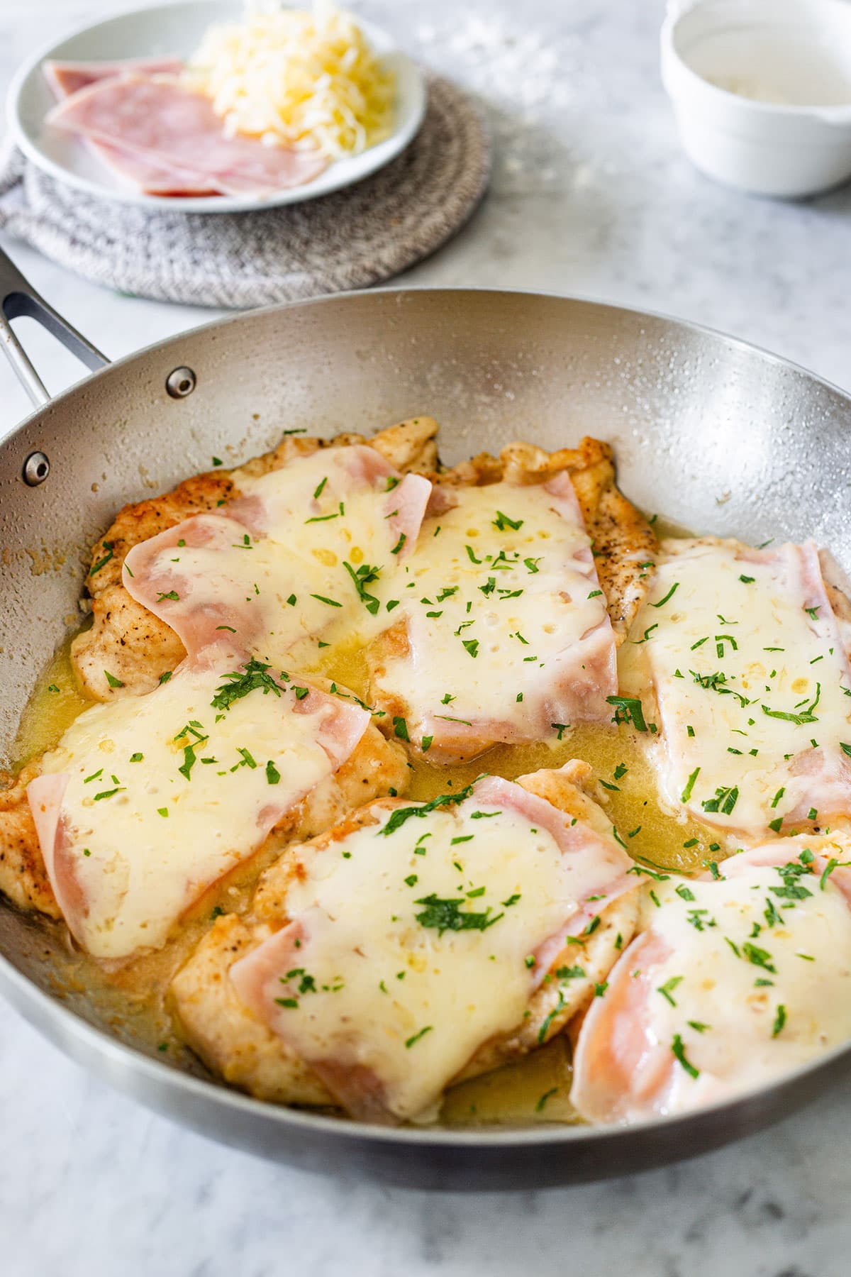 Valdostana chicken, also known as pollo alla Valdostana in a pan and a plate in the background with ham and cheese.