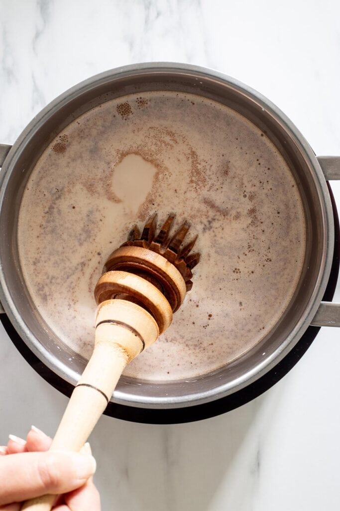 Mixing to dissolve the chocolate tablets into the hot milk.