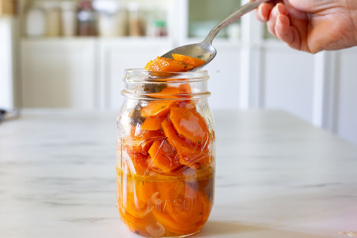 Placing the pickled carrots (zanahorias en escabeche) into a mason jar.