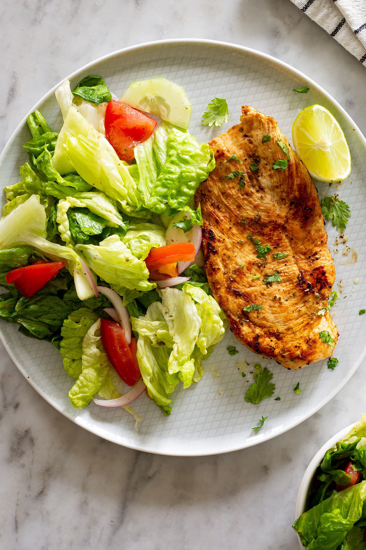 Grilled chicken breasts, known as pechugas de pollo a la plancha, on a plate with green salad.