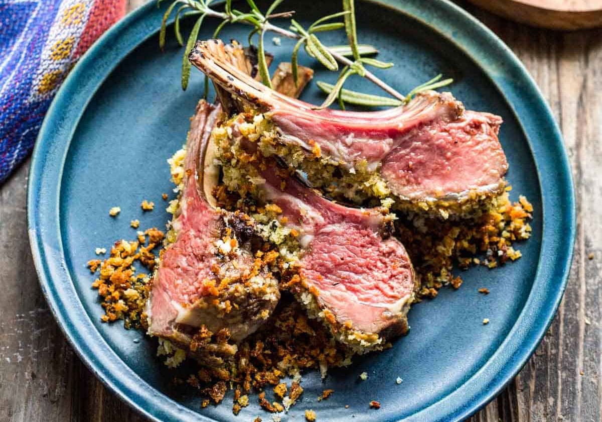 Dijon herb crusted rack of lamb on a plate with garnish on top.
