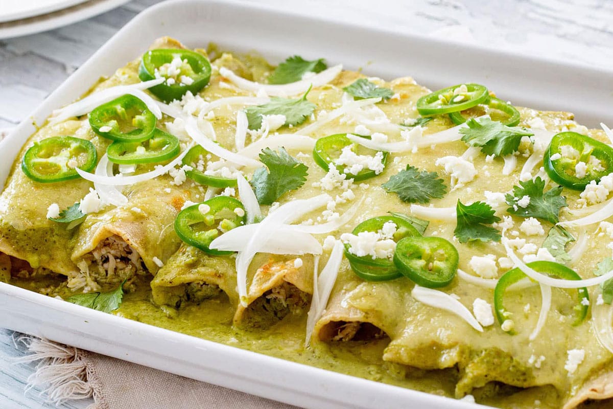 Enchiladas suizas verdes on a serving pan with garnish on top.