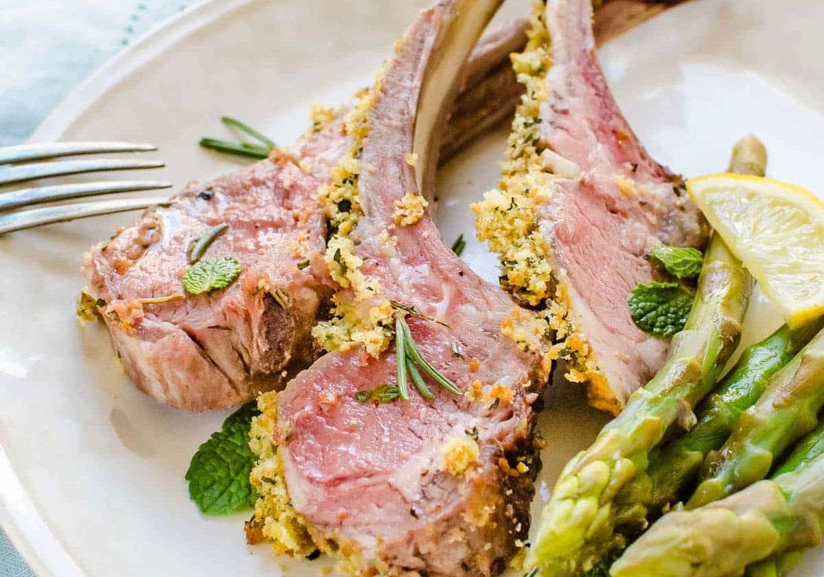 Herb crusted rack of lamb on a plate with garnish on top.