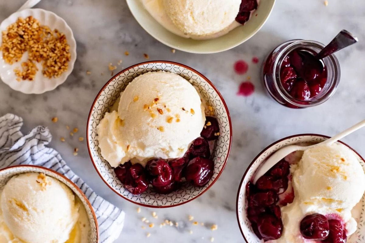 Four bowls of mascarpone ice cream topped with cherries and nuts.