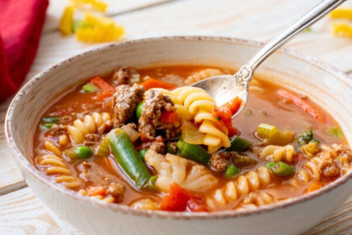 A bowl of soup with beef, pasta and veggies.