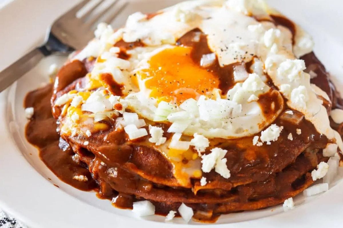 Stacked enchilads on a plate with egg and garnish on top.