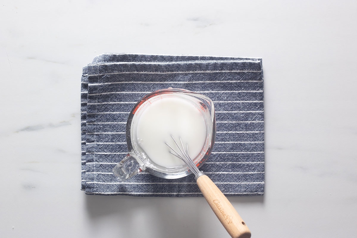 Cornstarch mixed with water in a cup and a whisk inside.