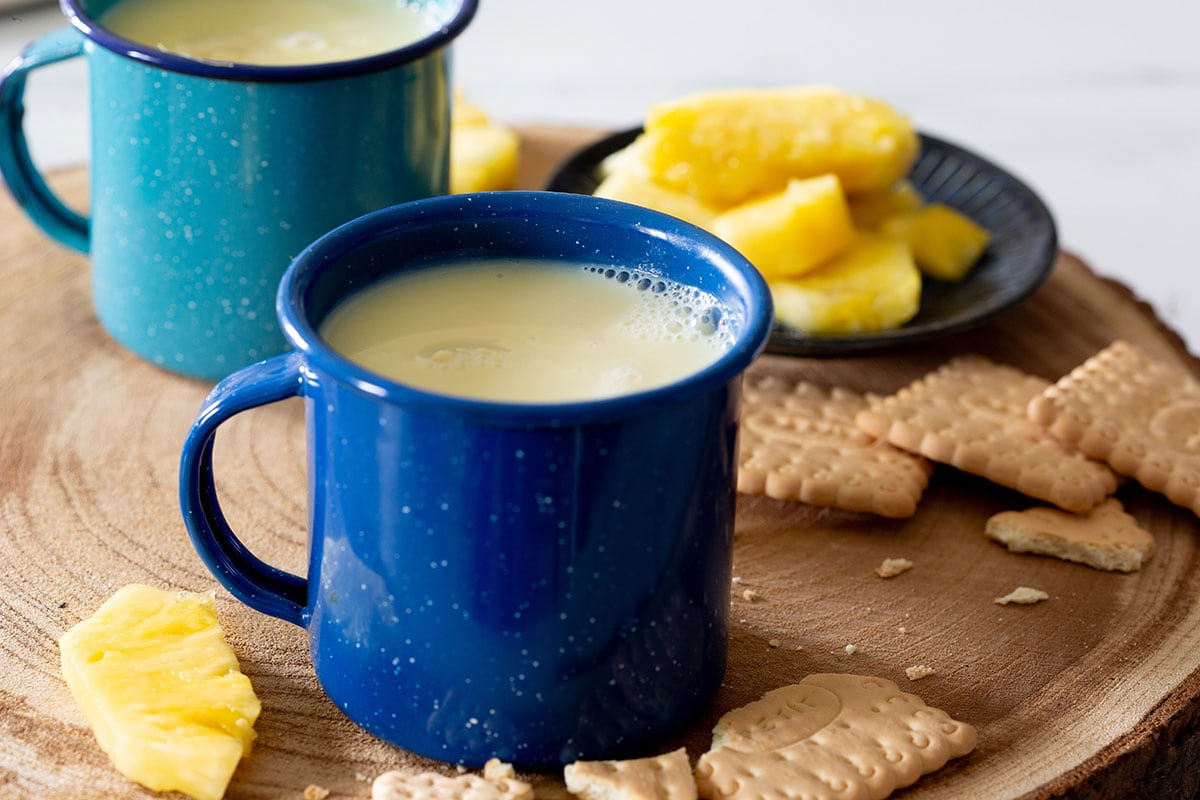Atole de piña served in cups and some cookies on the side.
