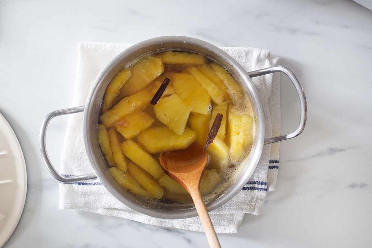 Cooked pineapple chunks in a pot with a wooden spoon.