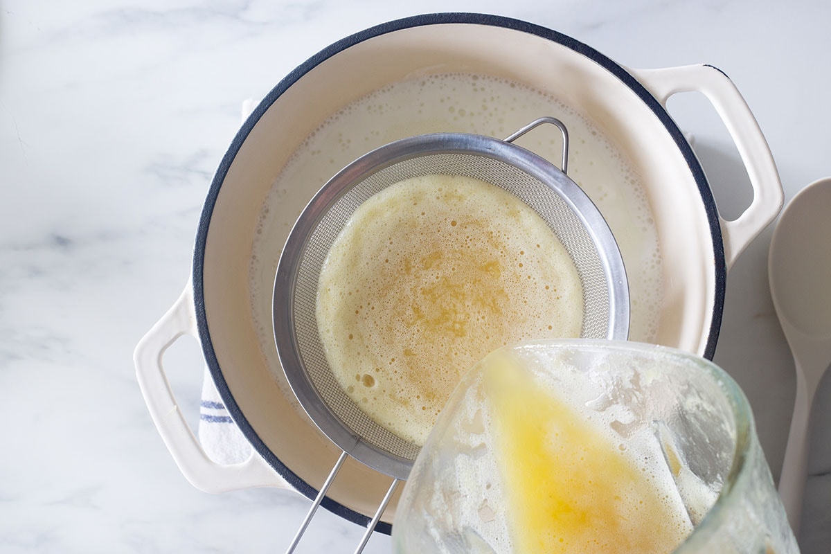 Straining the pineapple mixture into the pot with milk.