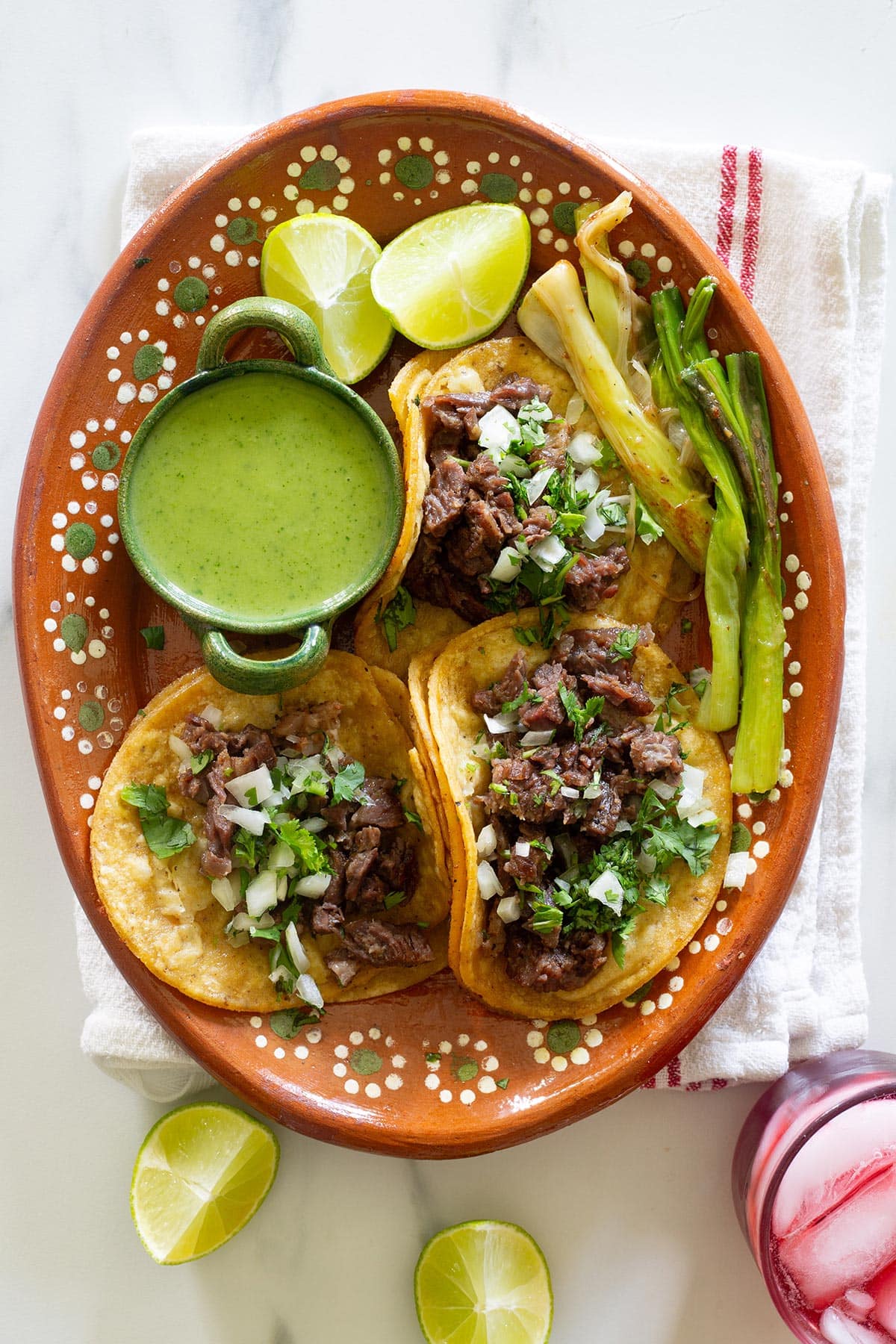 Tacos de Costilla de res in a platter with salsa guacamole, lime wedges, and onions.