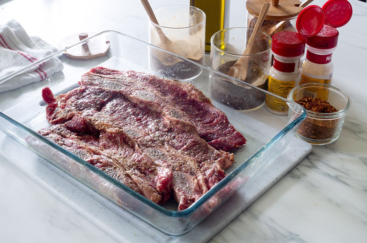 Beef ribs (costillas de res) seasoned in a glass container.