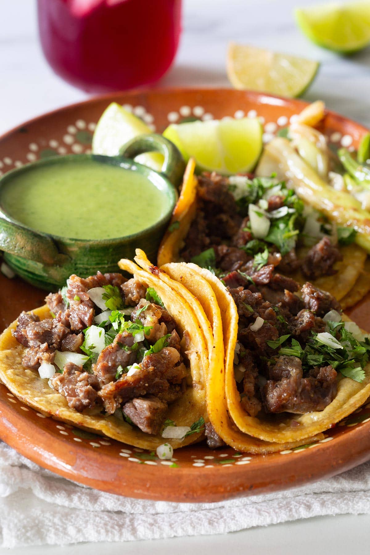 Tacos de Costilla de Res in a plate with lime wedges, salsa, and spring onions.