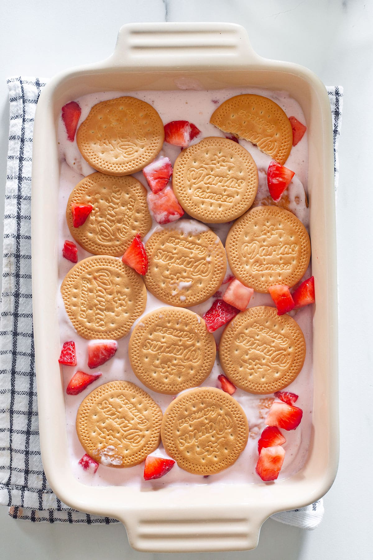 The layers of Maria cookies, strawberry cream, and fresh starwberries in a baking dish.