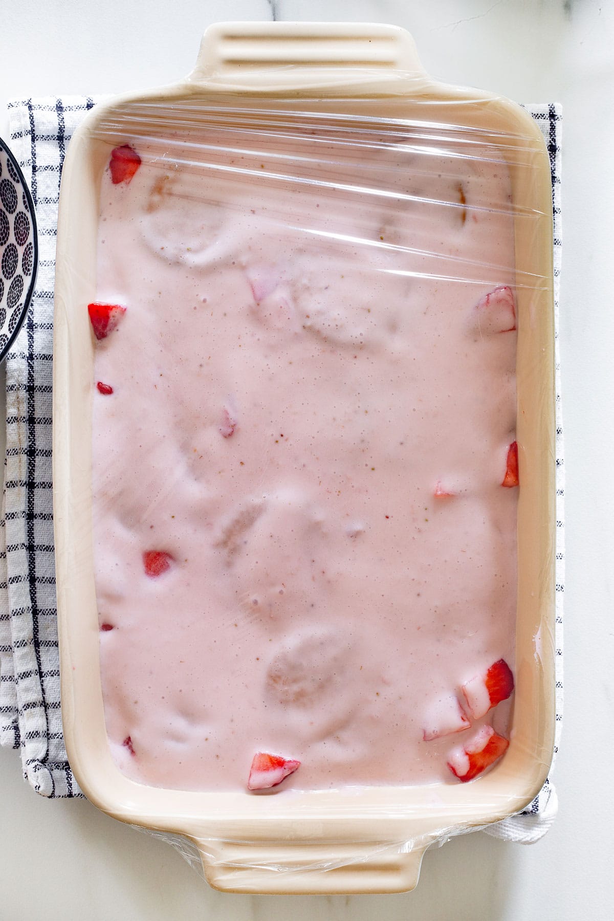 The dish with Carlota de Fresas covered with plastic wrap ready to refrigerate.