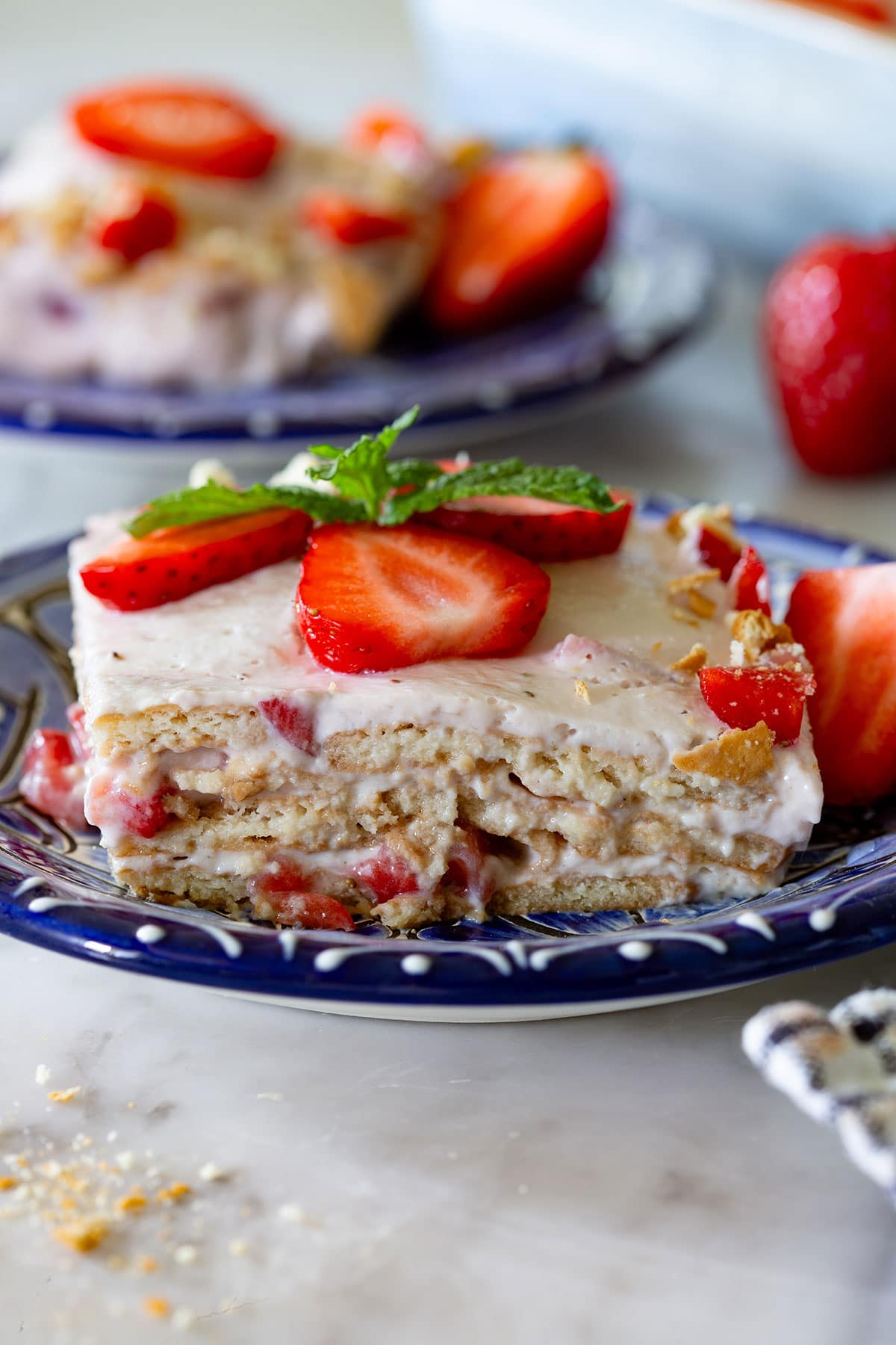 A portion of Carlota de Fresa in a small plate to show the creamy layers of Maria cookies, strawberries, and cream.