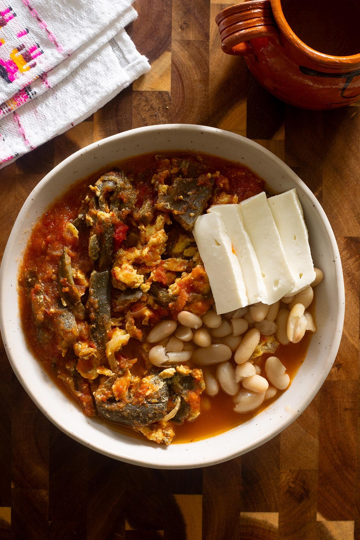 Rajas con huevos served in a plate with a side of beans and panela cheese. Tortillas and a cup of cafe de olla on the side too.