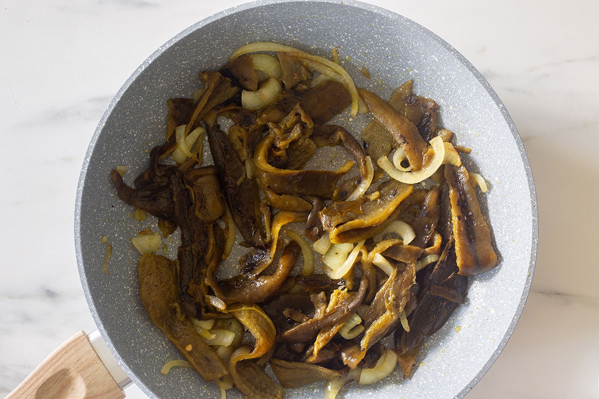Strips of poblano peppers cooking with onions in a pan.