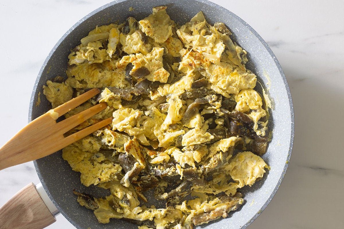 Poblano peppers, eggs, and onions fully cooked in a pan.