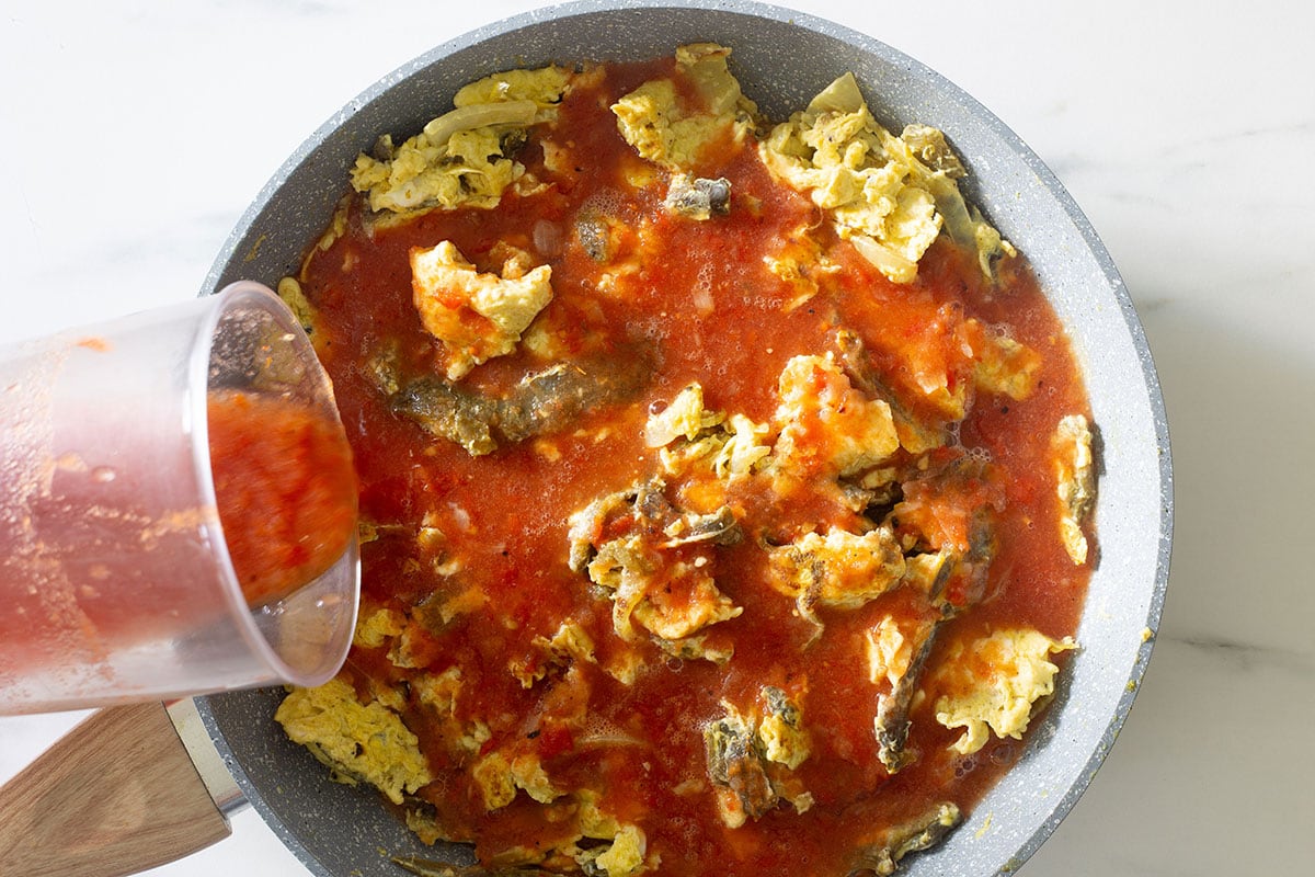 Pouring the salsa into the pan with eggs and poblano peppers rajas.