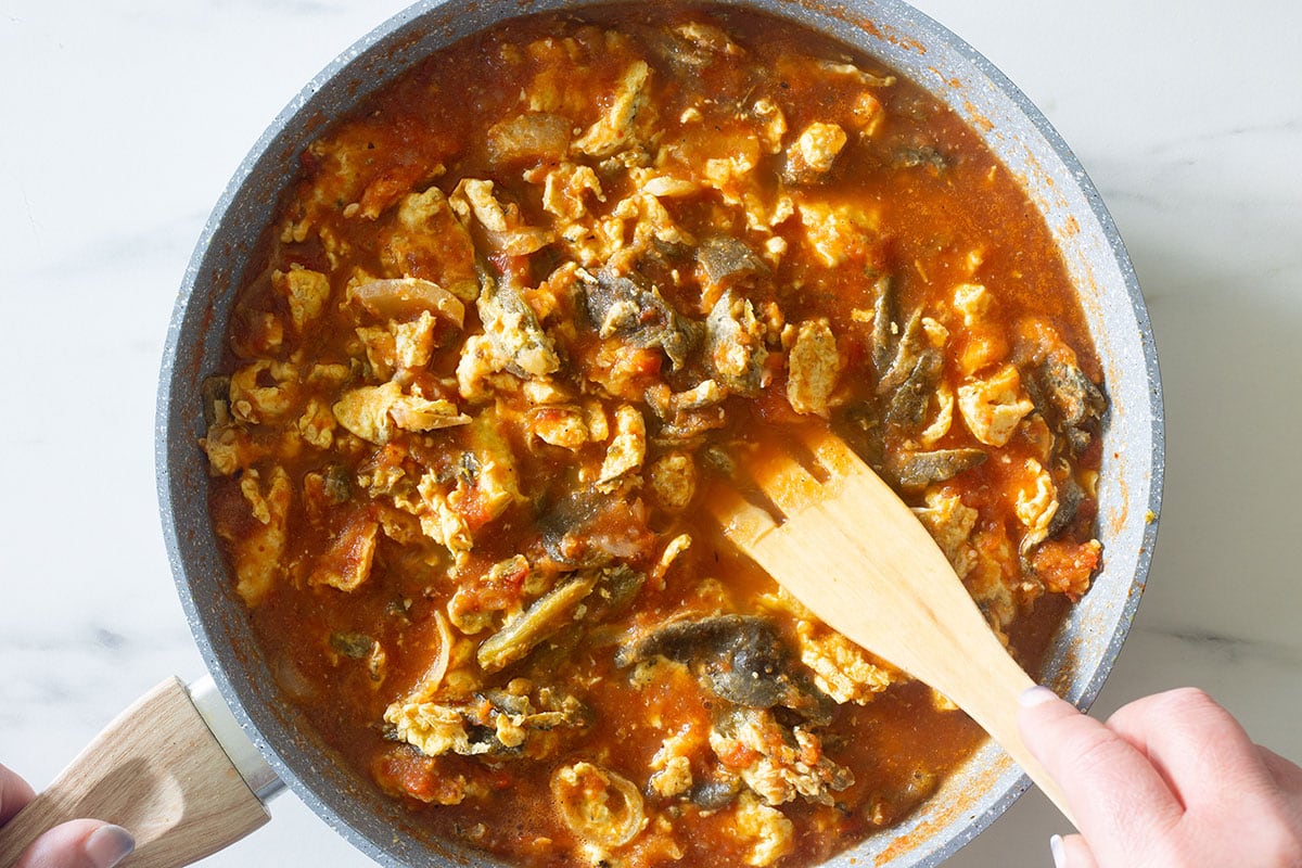Cooked rajas (strips) of poblano peppers with eggs and salsa in a pan.