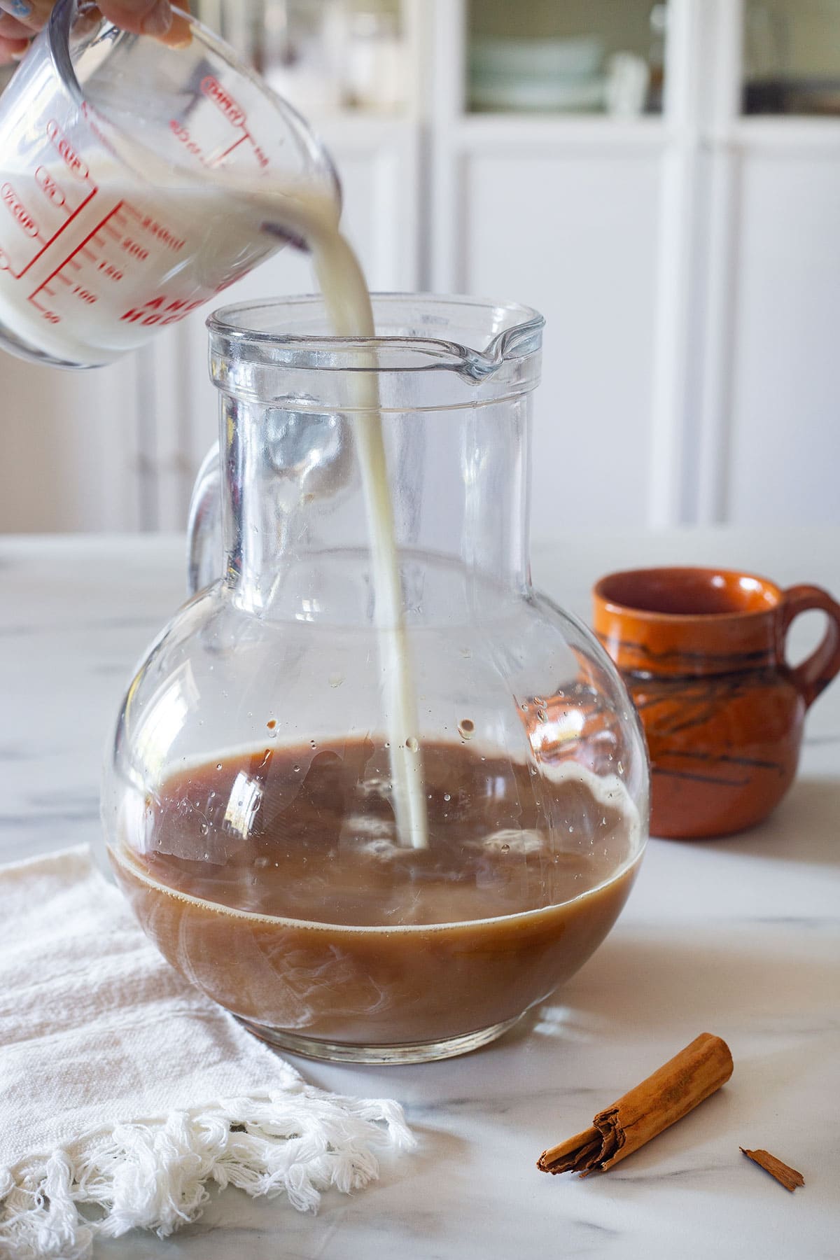 Adding evaporated milk to a pitcher with coffee.
