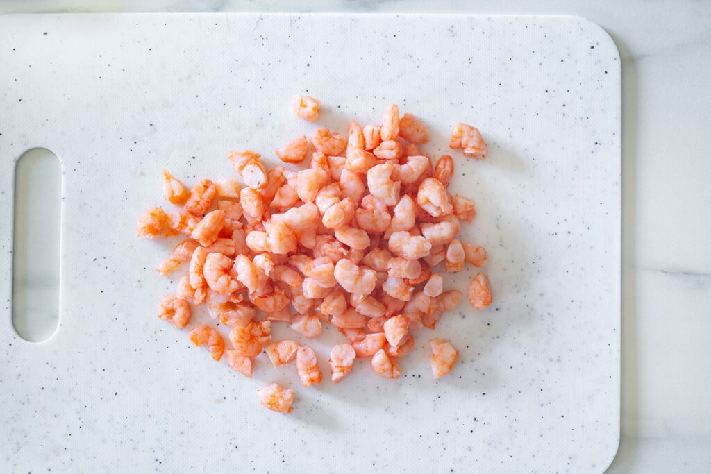 Shrimp cooked and cut into small pieces on a cutting board.