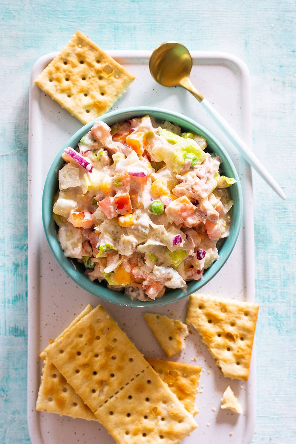 Ensalada de atún mexicana en un tazón turquesa con galletas saladas al lado.
