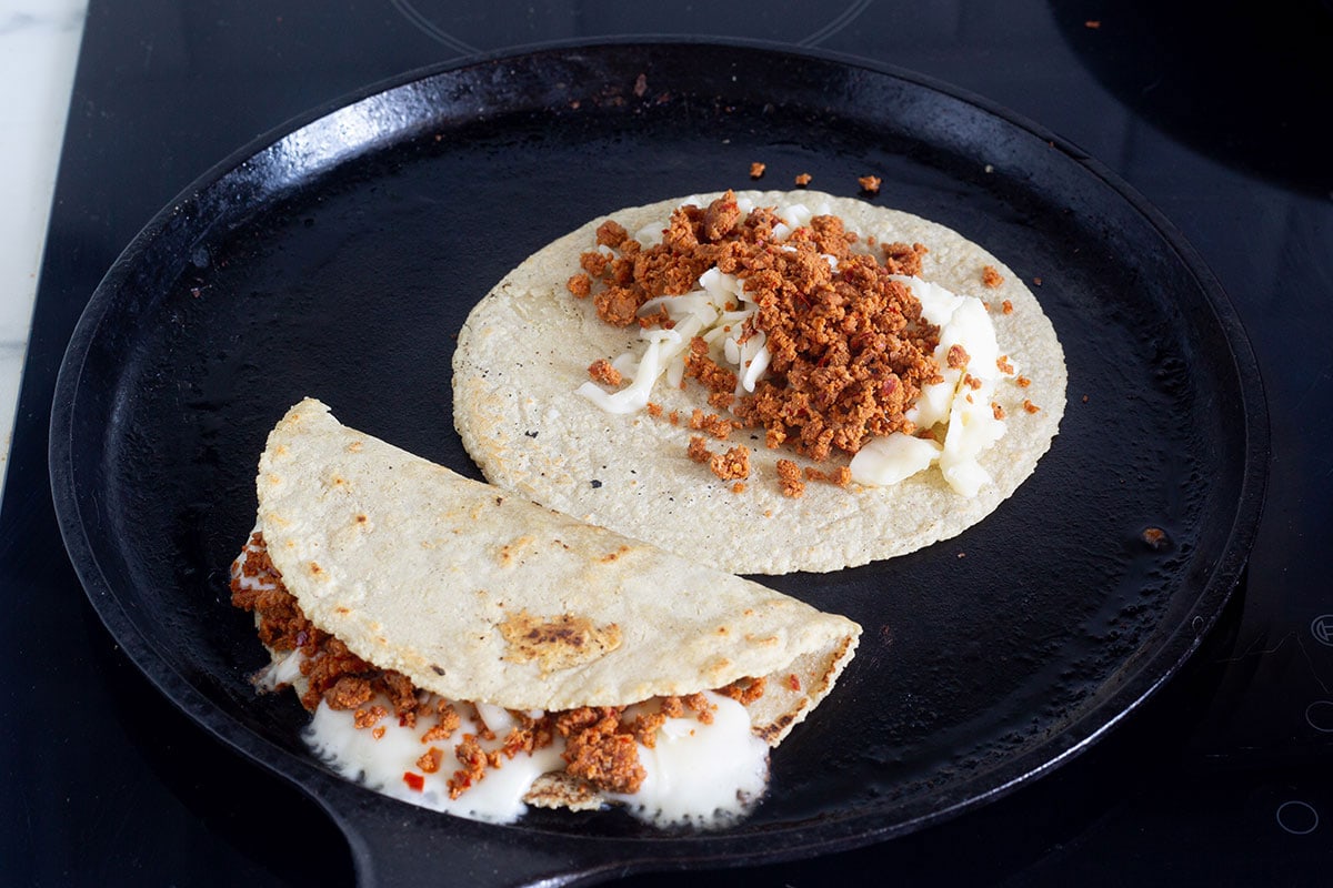 Folded chorizo quesadilla and a tortilla qith cheese and chorizo on a griddle.